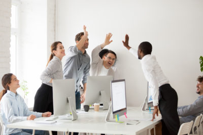 Happy multi-ethnic employees sales team giving high five together celebrating corporate success and good relations, diverse group of office people joining hands excited by common victory achievement